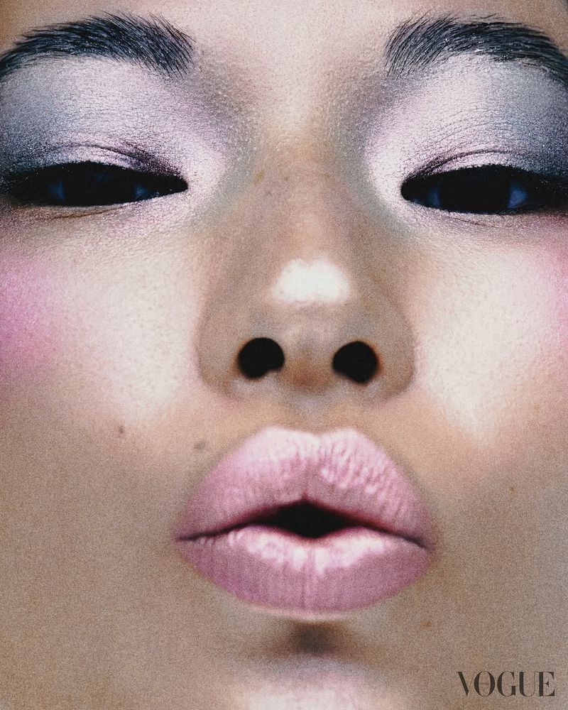Close-up of Asian woman's face with silver eyeshadow, pink blush, and pink lipstick puckering her lips in a beauty advertisement.