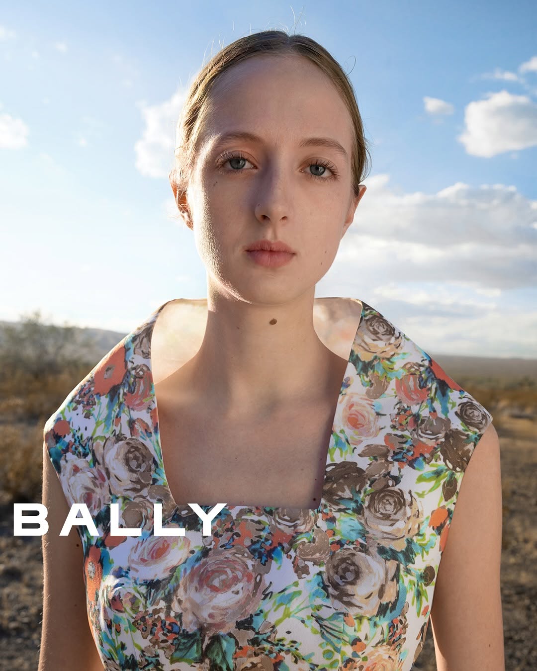Close-up of a woman in a floral dress against a desert and sky backdrop, fashion shoot, natural lighting, outdoor setting.