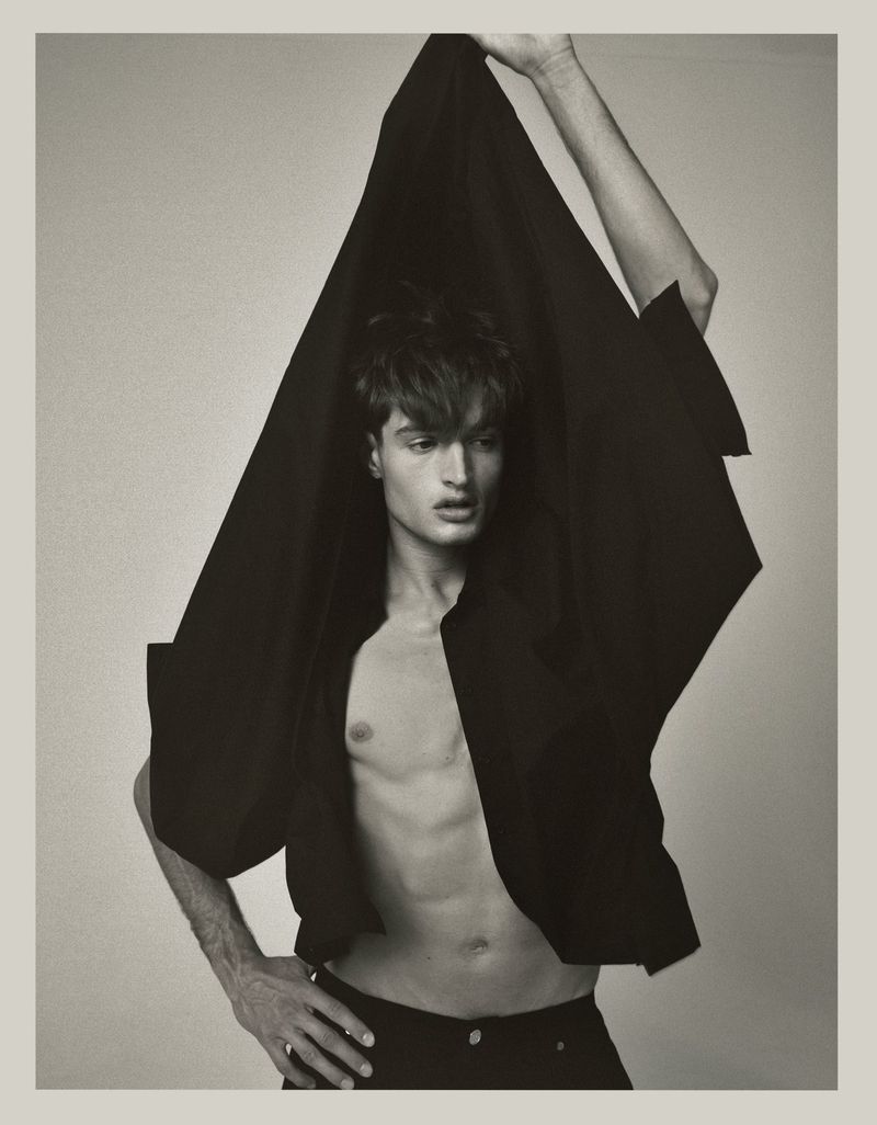 Monochrome portrait of a young adult male partially draped in black fabric against a light backdrop, showcasing a dramatic pose.