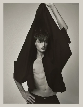 Monochrome portrait of a young adult male partially draped in black fabric against a light backdrop, showcasing a dramatic pose.