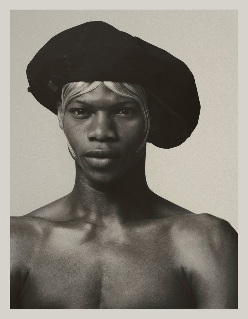 Striking portrait of a Black person wearing a black beret and pale wig, captured in a studio with a monochromatic color scheme.