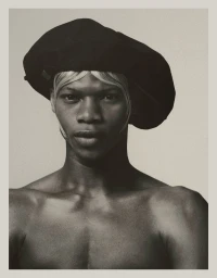 Shirtless Black male model Razak Salifou wearing an oversized black beret with blonde fringe against a studio backdrop.