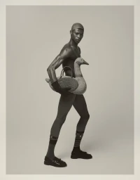 Black male model holding a woven duck bag against a neutral studio background for GQ Portugal Dressed and Naked editorial.
