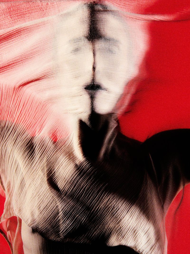Abstract image of a person's face obscured by textured fabric against a vibrant red background, creating a surreal, artistic effect.