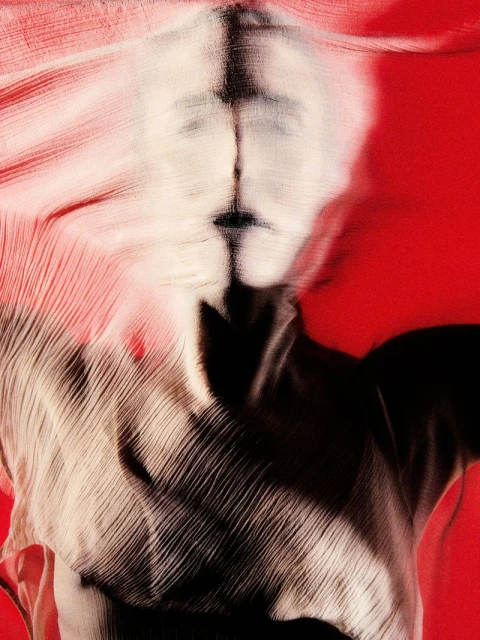 Abstract image of a person's face obscured by textured fabric against a vibrant red background, creating a surreal, artistic effect.