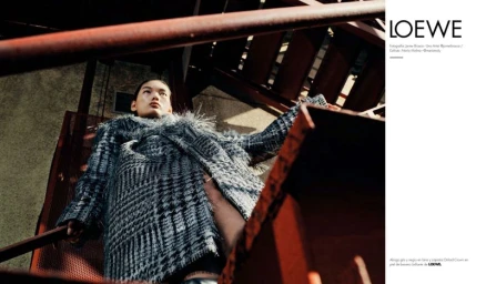 Model Xiaorui Li wearing a textured grey plaid coat poses on a rusty metal staircase in bright sunlight.