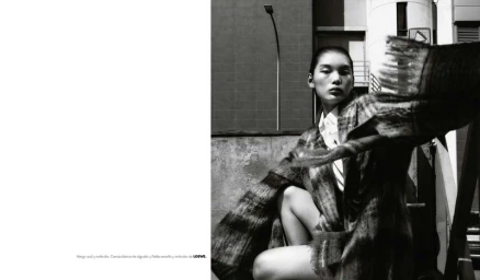 Monochrome fashion editorial image featuring a model in a patterned coat against an urban architectural backdrop.