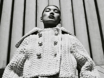 Low-angle monochrome portrait of a model wearing a textured double-breasted knit jacket with large metallic buttons.