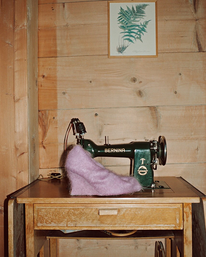Vintage sewing machine with purple fabric on a wooden table in front of a wooden wall with a fern print.