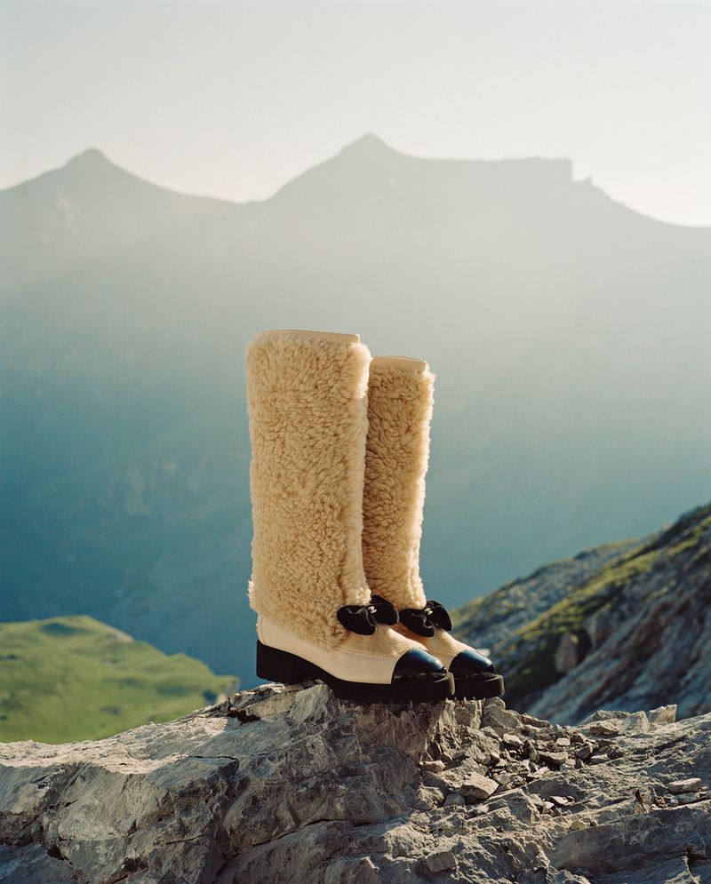 Fashionable shearling boots displayed on a rocky surface with a mountain range backdrop under soft, natural light.