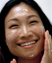 Close-up portrait of a smiling woman applying white gel cream to her face for the Mecca Cosmetica campaign