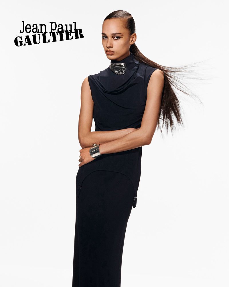 Elegant Black Dress Fashion: Woman in sleeveless black high-neck gown and silver cuff bracelet against a bright white backdrop, fashion-forward.