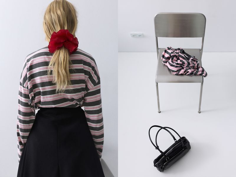 Blonde woman in a striped top and black skirt, with a large red scrunchie, stands near a chair with a patterned top and a black purse.
