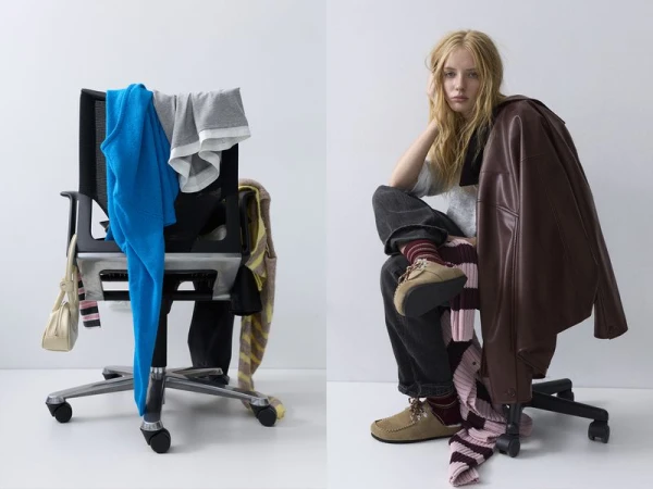 Indoor shot of an adult female sitting on a chair next to a chair with clothing draped over it in front of a white wall.