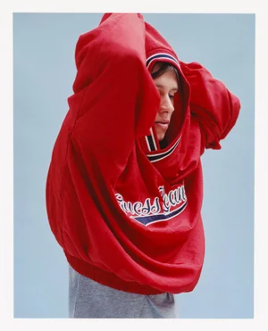 Model wearing a red hooded sweatshirt with white trim against a plain light blue background.
