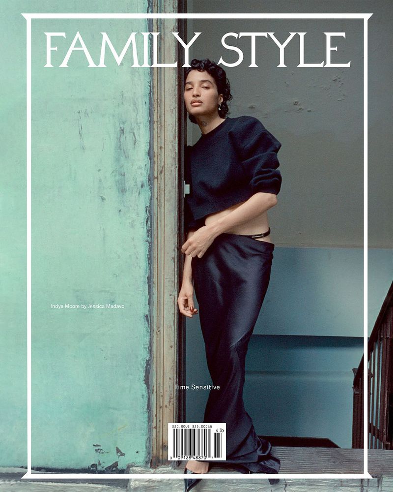 Magazine cover features a woman in a black top and long skirt, leaning against a blue-green wall next to a doorway with visible stairs.