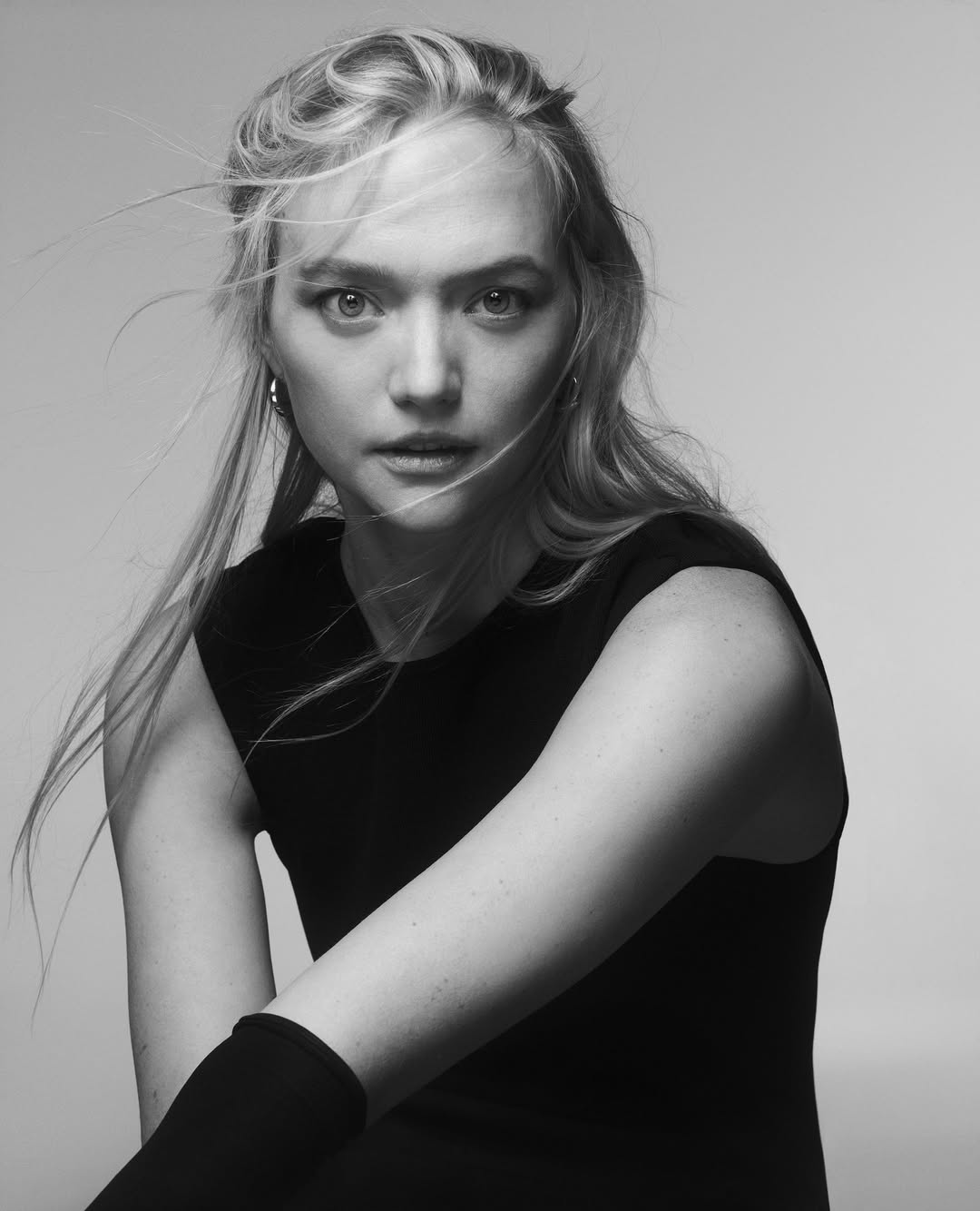 Black and white portrait of a blonde woman with long hair, wearing a black top. Studio shot with a neutral background.