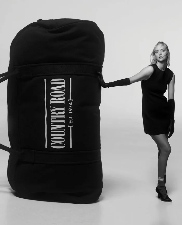 Model Gemma Ward leaning against an oversized black Country Road duffel bag in a studio setting