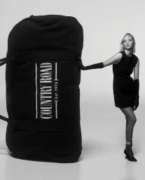 Model Gemma Ward leaning against an oversized black Country Road duffel bag in a studio setting