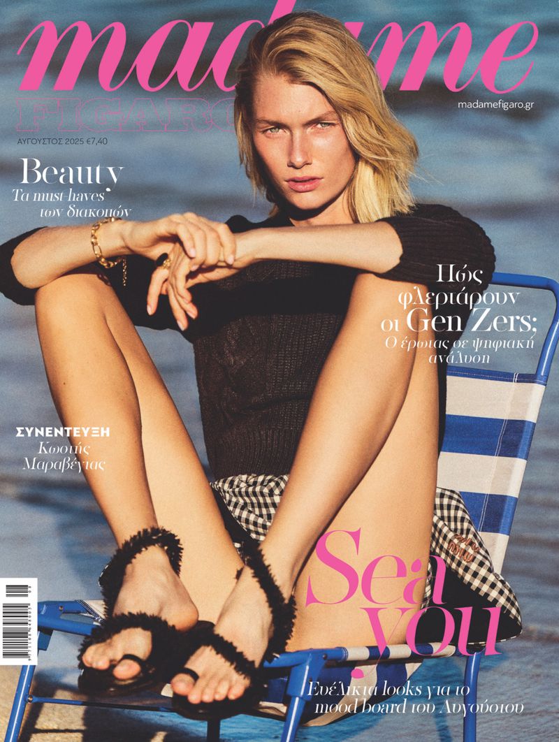 Magazine cover featuring a model sitting on a beach chair. Blonde hair, wearing black top, patterned skirt, and black sandals.