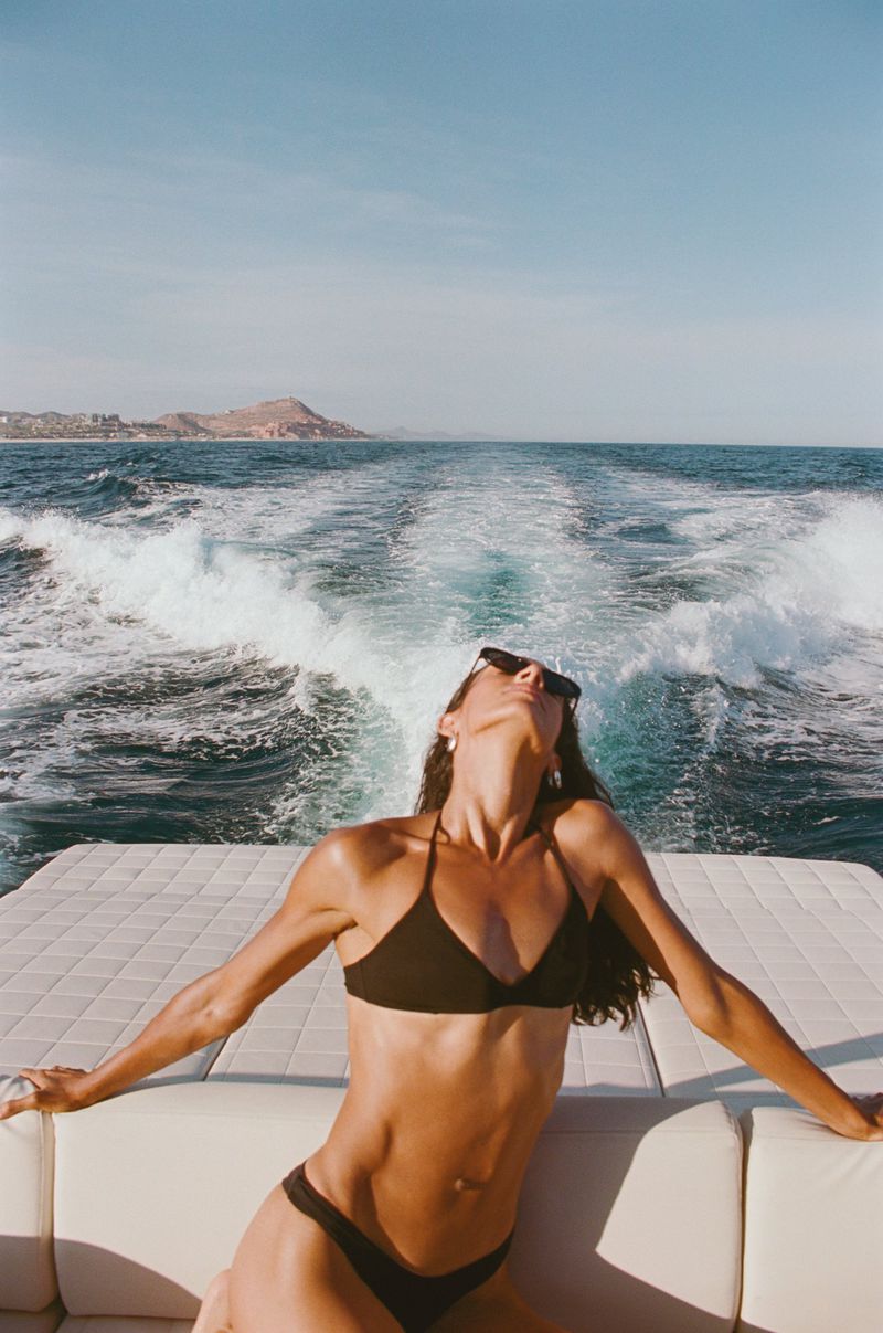 Woman in black bikini on boat with ocean view. Enjoying summer vibes, sunbathing on a yacht, luxury travel experience.