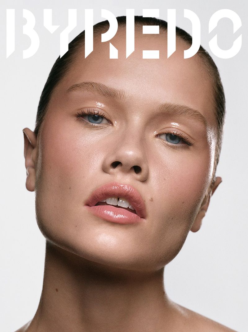 Close-up portrait of a woman with glossy makeup on a light background, featuring the Byredo logo.