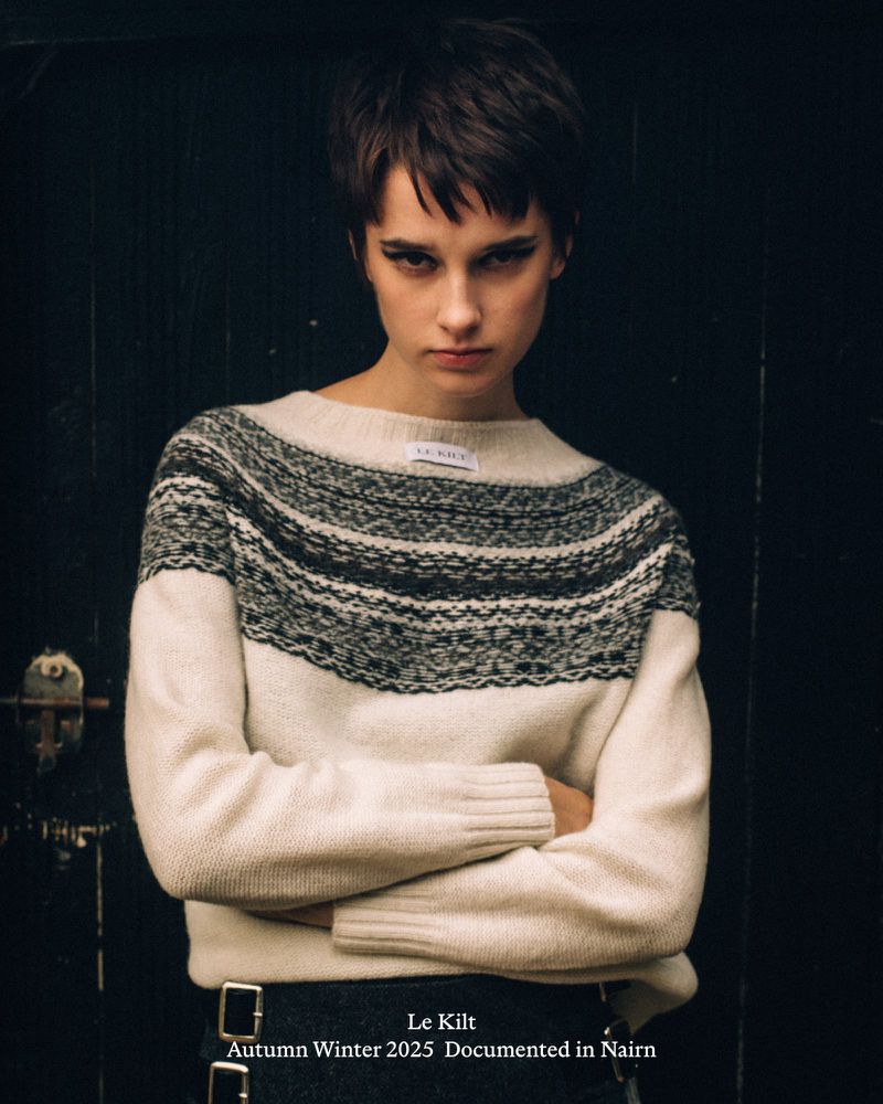 Fashion editorial image of a young woman in a patterned sweater with arms crossed against a dark background, showcasing winter apparel.