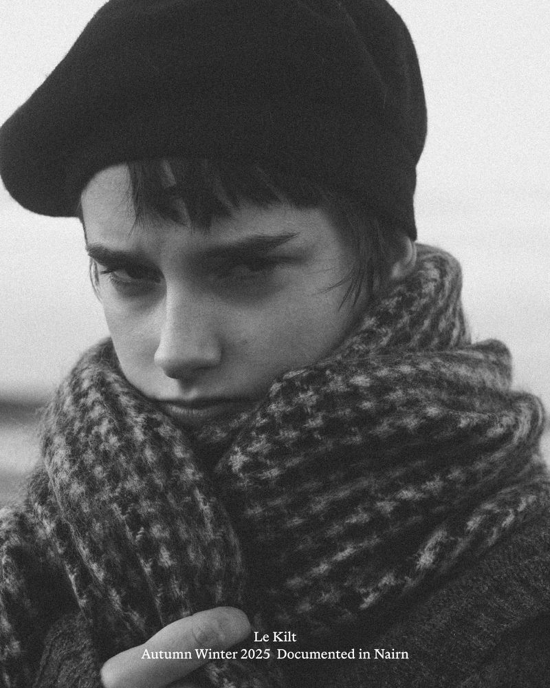 Monochrome close-up of a young adult wearing a beret and scarf, with a neutral expression in an outdoor setting.