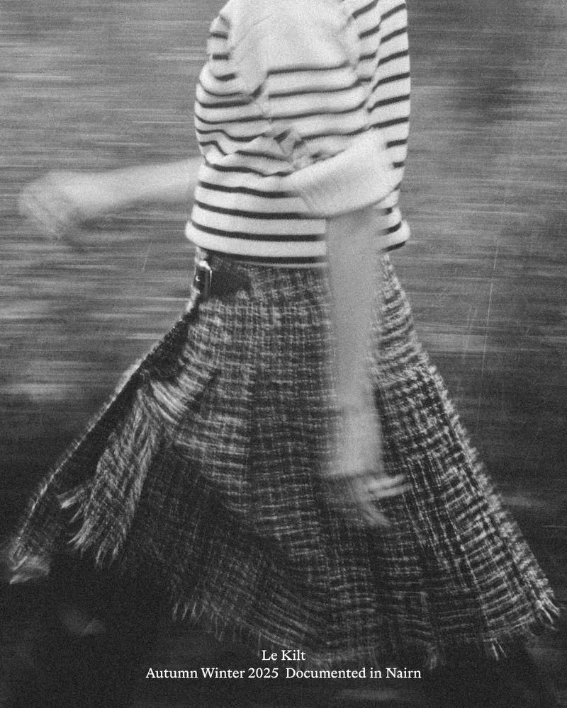 Fashion shot of a model wearing a striped top and kilt-style skirt with blurred motion in an outdoor setting; black and white photography.