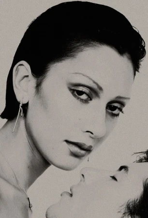 Close-up monochrome portrait of two people with slicked-back dark hair and dramatic makeup against a light background.