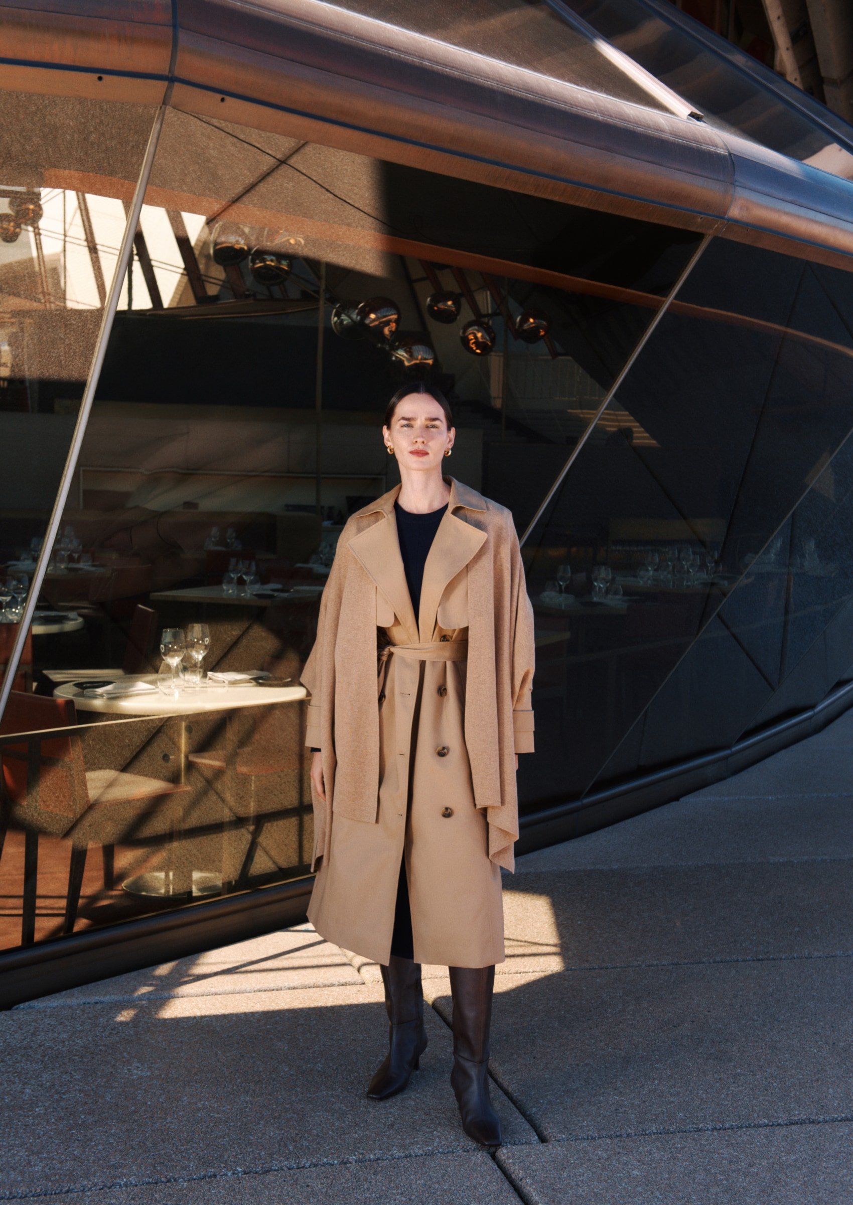A full-length shot captures a stylish woman in a trench coat and boots, posing outdoors against a modern architectural backdrop.