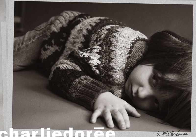 Child with dark hair wearing a patterned sweater resting on a table in a subdued, vintage-toned studio portrait with soft lighting.
