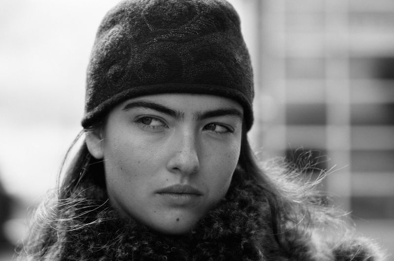 Black and white portrait of a woman with a knit cap and a fur collar, looking off to the side against an out-of-focus background.