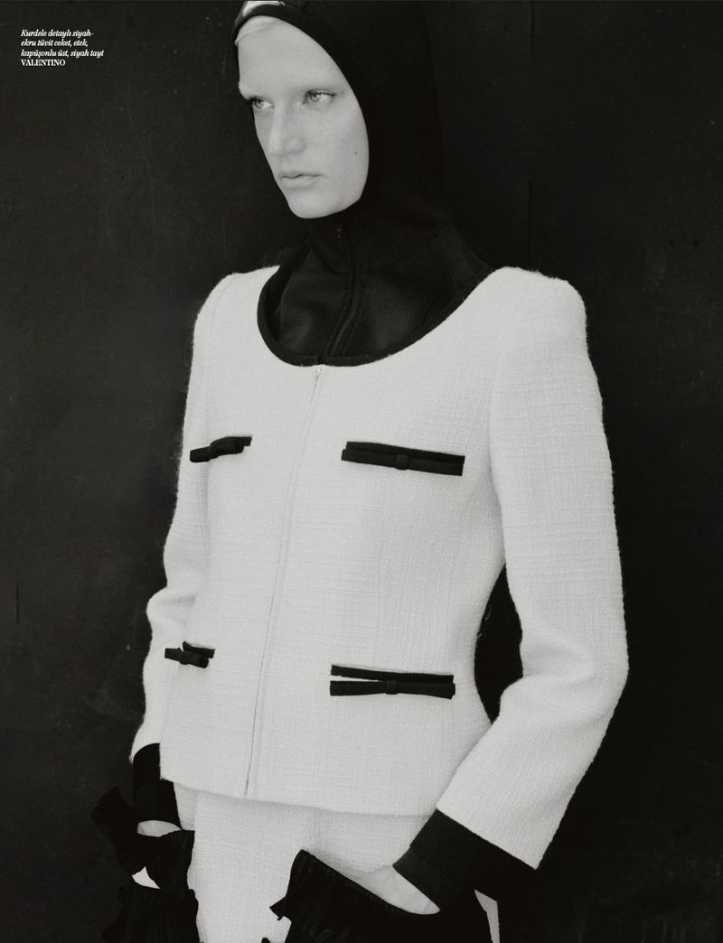 Monochromatic fashion editorial shot of a woman wearing a white boucle jacket with black accents against a dark background in a studio.