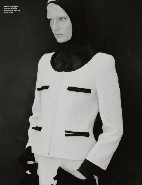 Monochromatic fashion editorial shot of a woman wearing a white boucle jacket with black accents against a dark background in a studio.
