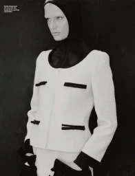 Model Michelle Laff wearing a white textured jacket with black trim and a black hood against a dark background.