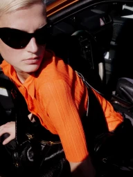Model in dark sunglasses and vibrant orange top posing inside a car for Vogue Turkey editorial