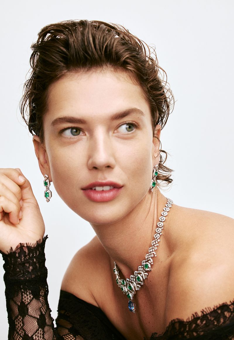 Close-up of a woman wearing a diamond and emerald necklace and matching earrings in a light studio setting, beauty and fashion.