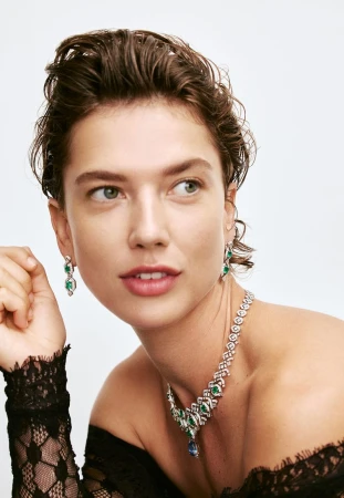 Close-up of a woman wearing a diamond and emerald necklace and matching earrings in a light studio setting, beauty and fashion.