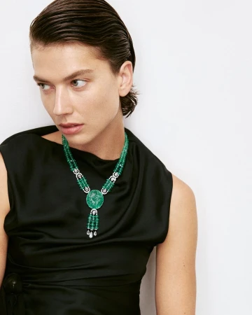 Close-up of a woman wearing a black dress and an elaborate green beaded necklace with a medallion and diamond accents.