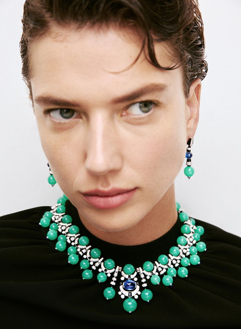 Close-up of a woman wearing a green beaded necklace and matching earrings against a bright white background in a beauty shot.