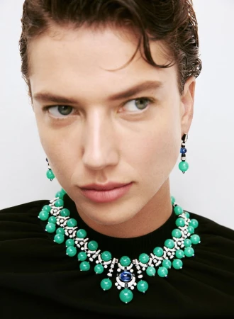 Close-up of a woman wearing a green beaded necklace and matching earrings against a bright white background in a beauty shot.