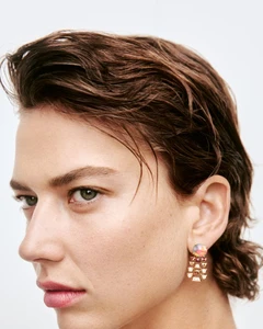 Close-up profile of model Gigi Ringel with wet-look brown hair wearing a gemstone drop earring against a white background.