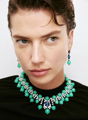 Model Gigi Ringel wearing an elaborate green beaded Cartier necklace and matching earrings against a white background.