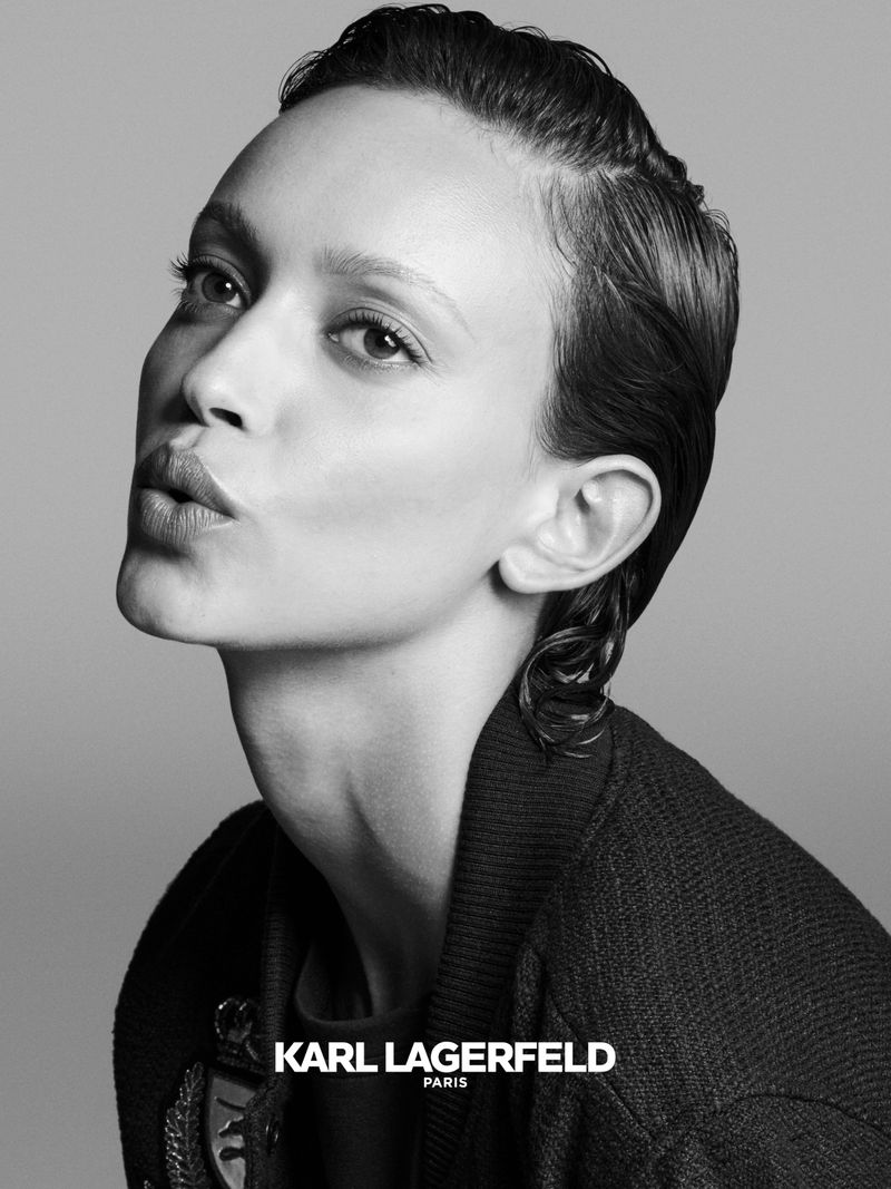 Striking black and white portrait of a young adult woman with styled hair and a neutral expression wearing a dark jacket.