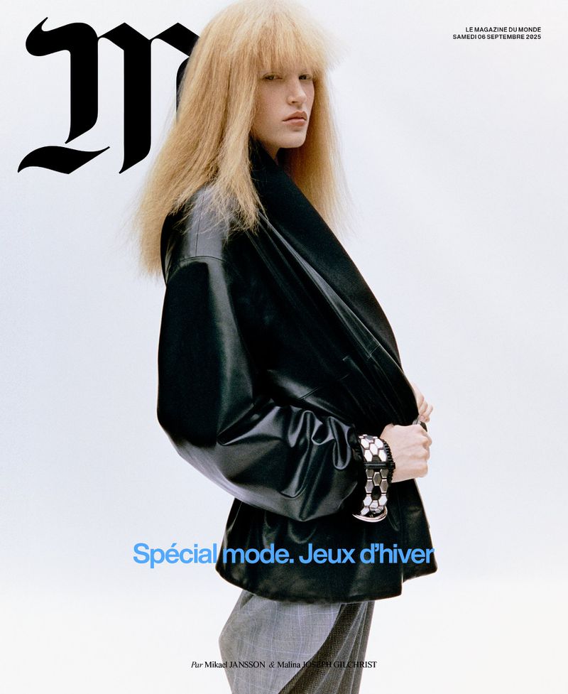 Blonde fashion model in an oversized black leather jacket and grey trousers against a bright white studio backdrop for a magazine cover.