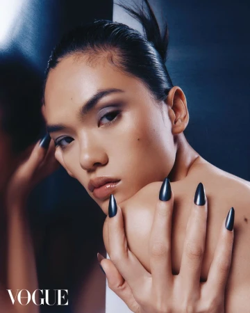 Close-up beauty shot of an Asian female model with long, black nails, styled hair, and smokey eye makeup, posing in a studio.