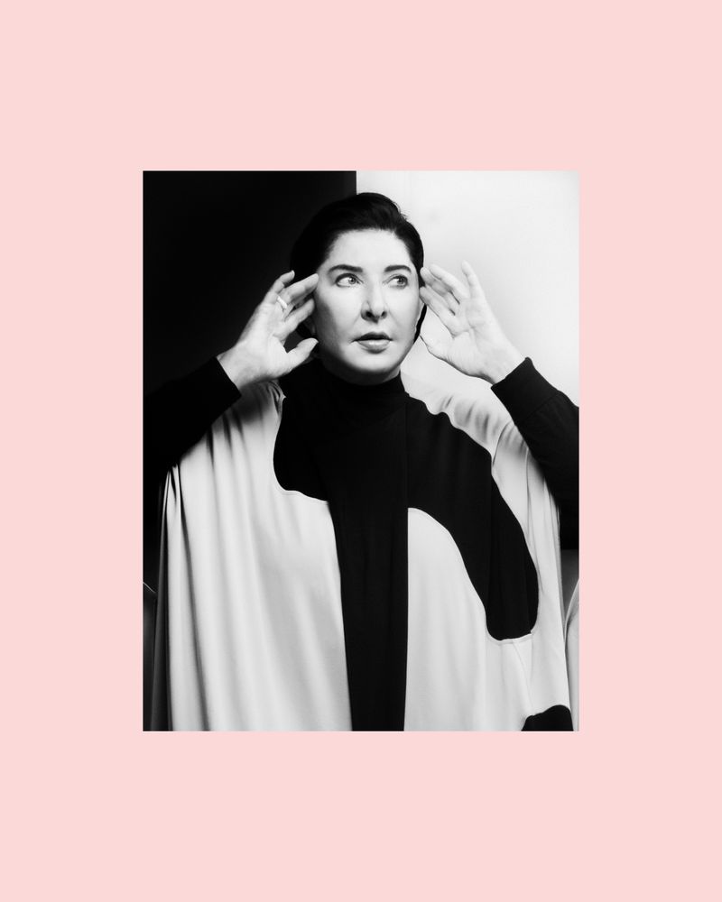 Monochrome portrait of a woman with hands near her ears, wearing a black and white poncho against a contrasting background.