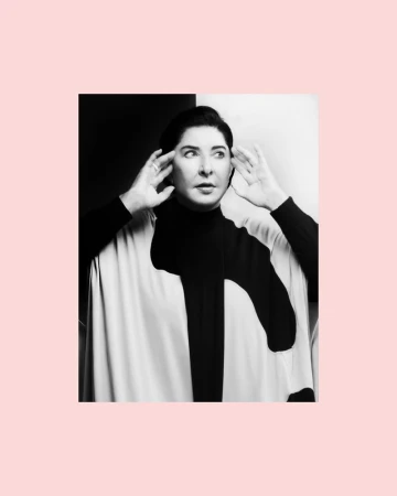 Monochrome portrait of a woman with hands near her ears, wearing a black and white poncho against a contrasting background.