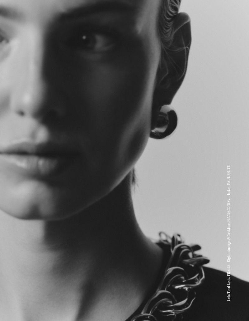 Monochrome portrait of a model showcasing a chunky chain necklace and earring against a plain background in a high-fashion studio setting.